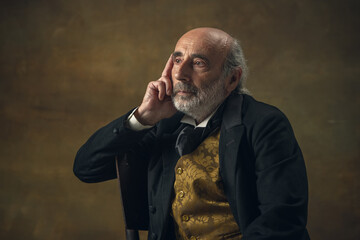 Half-length retro portrait of sad elderly gray-haired man, gentleman, aristocrat or actor isolated on dark vintage background. Retro style, comparison of eras concept.