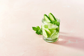 Fresh summer detox and refreshing drinks with cucumber, lime, mint on white wall background. Sunny day shadows from mocktail on pink surface.