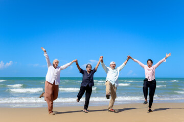 Obraz premium Group of four cheerful elderly old senior friends travel outdoor together, holding and raising hands while standing on beach, have fun and enjoy spend time, resting and relaxing on holiday vacation.