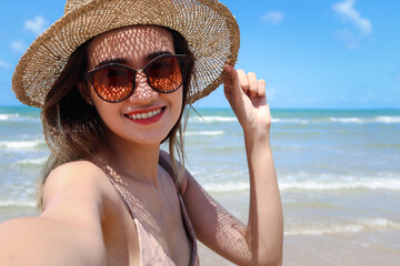 Portrait of beautiful Asian woman with big hat and sunglasses enjoy spending time on tropical sand beach blue sea, happy smiling female resting and relaxing on summer holiday vacation.