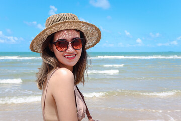 Portrait of beautiful Asian woman with big hat and sunglasses enjoy spending time on tropical sand beach blue sea, happy smiling female resting and relaxing on summer holiday vacation.