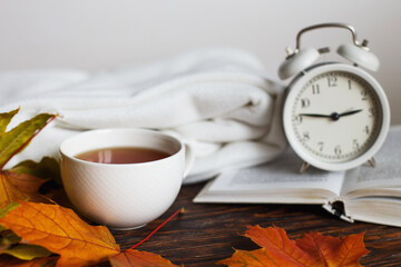 Naklejka na ściany i meble cup of coffee or tea with golden autumn leaves, plaid, alarm clock and book on a wooden background .Fall concept.
