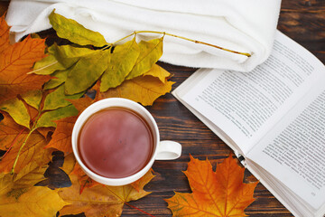 cup of coffee or tea with golden autumn leaves, plaid and book on a wooden background .top view. Fall concept.