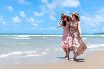 Two beautiful Asian women with big hat and sunglasses enjoy spending time with friend on tropical...