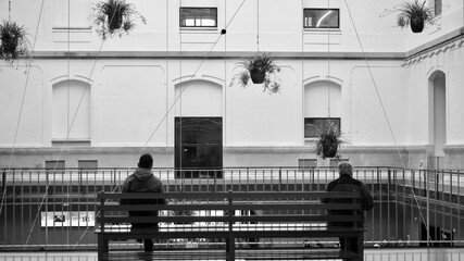 Grayscale shot of two people sitting on the opposite sides of a bench inside of a building