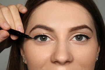 Artist applying black eyeliner onto woman's face on grey background, closeup