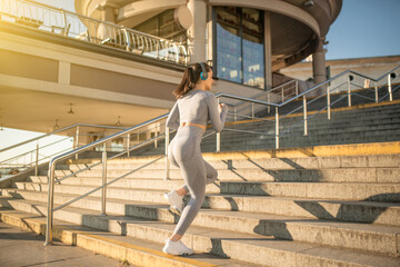 Sporty girl in grey sportswear having cardio on the stairs