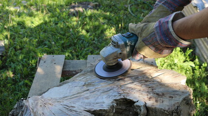 surface treatment of a part of the stump with an angle saw in gloved hands in the open air,...
