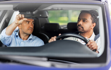 driver courses and people concept - man and driving school instructor adjusting mirror in car