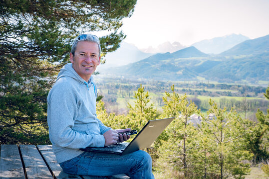 Homme qui travaille avec son ordinateur et son téléphone en pleine nature devant un beau panorama et les montagnes