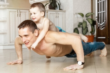 Dad and son do push-ups from the floor in the room of the house. The child lies on his father's...