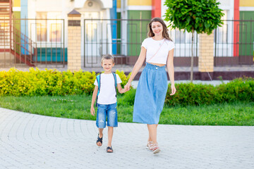 mom leads her son's child by the hand with a backpack to school or kindergarten, and back to school