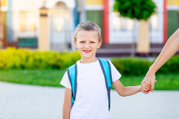 a child boy goes with a backpack to school or kindergarten by the hand with a parent mom and...