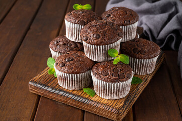 Chocolate muffins or cupcakes with chocolate drops on a dark wooden background with fresh berries and mint. Copy space.