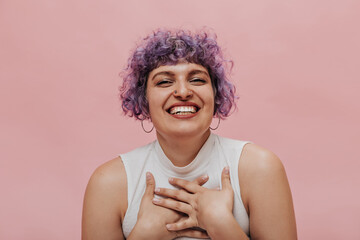 Sincere adult girl with wavy purple hair laughs on isolated backdrop. Woman with piercing posing in...