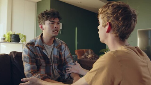 Young male gay couple sitting on couch explaining to each other in argument 