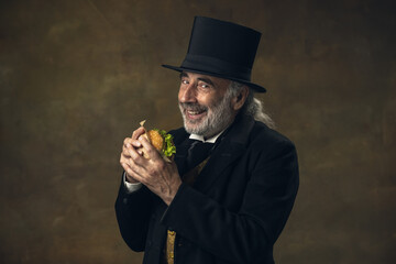 Handsome elderly gray-haired man, gentleman, aristocrat or actor eating fast food isolated on dark...