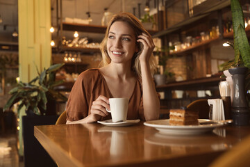 Young woman with cup of coffee at cafe in morning