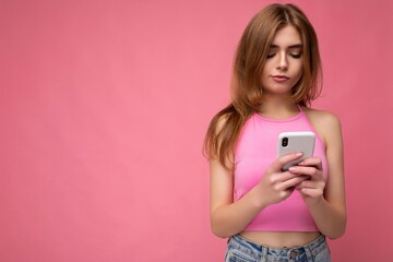 Beautiful young woman wearing casual clothes standing isolated over background surfing on the internet via phone looking at mobile screen