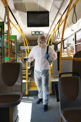 Fototapeta na wymiar Public transport sanitation. Worker in protective suit disinfecting bus salon