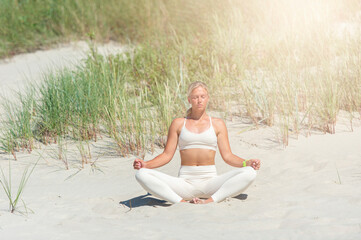 Fototapeta premium Woman practicing yoga on a sand dune on the beach
