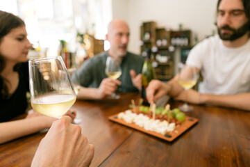 group of friends around a table joying wine food and company - focus on hand on the left holding wineglass