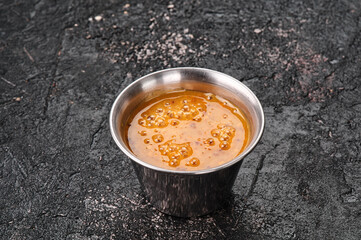 Mustard orange sauce in a metal gravy boat isolated on textured black background. Space for text. High quality photo