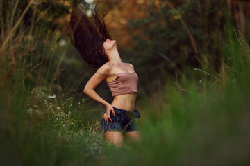 Sexy woman posing in a field in the grass rays of the sunset. Lifestyle on nature dressed in jeans...