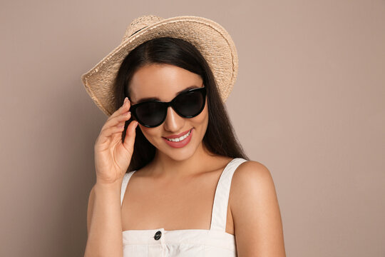 Beautiful young woman with straw hat and sunglasses on beige background. Stylish headdress