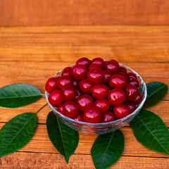 Ripe large juicy cherries in a transparent plate on a wooden table with green leaves.