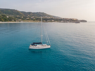 Aerial view of a sailboat moored off the coast of Calabria in Tropea. Italy. Tyrrhenian Sea. Coastline and blue sea
