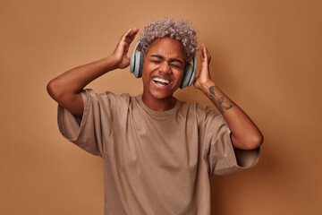 Happy curly haired African American female dances carefree sings favorite song listens music in...