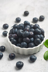 Organic blueberries in a white bowl on a concrete background with a leaf