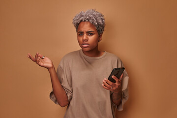 Angry African American young woman holding cellphone irritated by broken device malware poor...