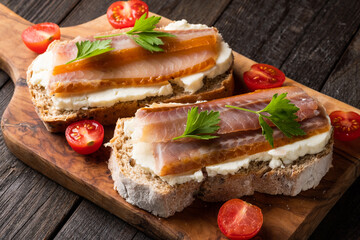 Sandwich with smoked fish, tomatoes, cream cheese  on bread, on a dark wooden table.