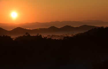 A huge of the sun rising over the mountains and forests. with a faint fog spread throughout the...