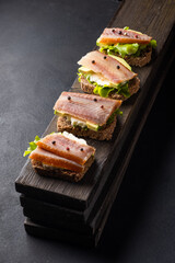 Sandwiches with smoked fish on a board on a dark background.