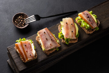 Sandwiches with smoked fish on a board on a dark background.
