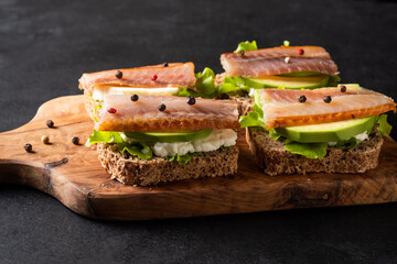 Sandwich with smoked fish, avocado, cream cheese, leaves salad  on rye bread. Snack on a dark wooden table.