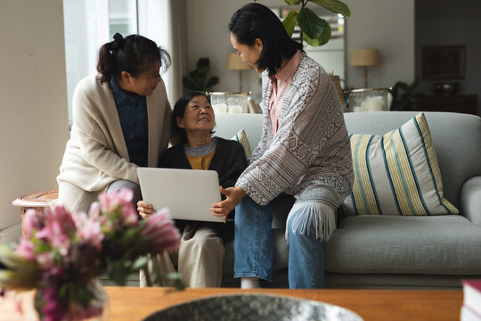 Happy senior asian woman at home with adult daughter and granddaughter using laptop