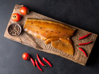 Smoked fish on a wooden board with tomatoes, peppers.