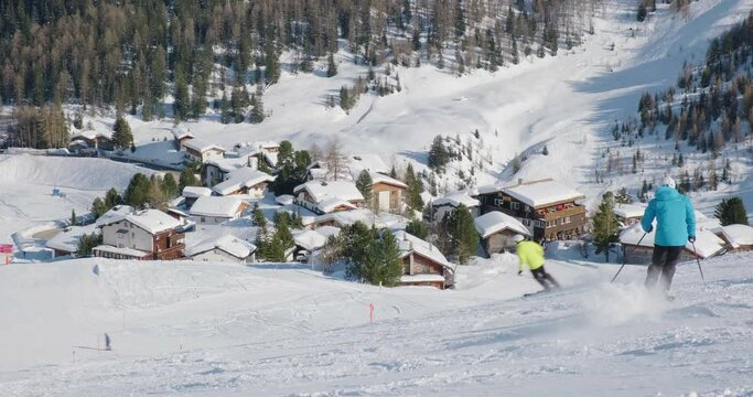 Winter sport activities with skiers on slopes at Arosa Lenzerheide ski resort, Switzerland. Ski season, mountain village, wooden huts covered with snow.