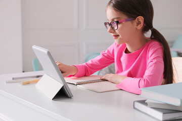 Little girl doing homework with tablet at table in room