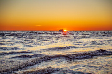 Gorgeous sunset in the Baltic Sea. At the horizon the yacht sails and the ship is about to enter the port.