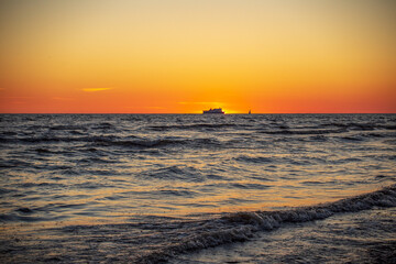 Gorgeous sunset in the Baltic Sea. At the horizon the yacht sails and the ship is about to enter the port.