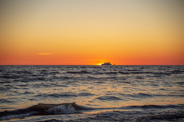 Gorgeous sunset in the Baltic Sea. At the horizon the yacht sails and the ship is about to enter the port.