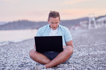 Man brunette with a laptop on a on the beach. Freelancer, working remotely, webinar, learning concept, chatting with friends. New normal concept.