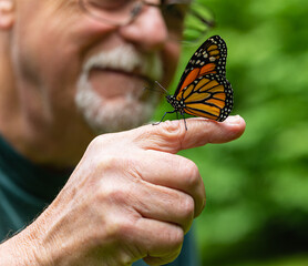 Senior male gazing at a monarch butterfly perched on his finger before he releases it into the wild.