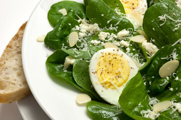 A healthy fresh spinach salad with almonds, hard boiled egg, feta, and a hard parmesan, romano style cheese