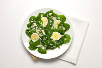 A healthy fresh spinach salad with almonds, hard boiled egg, feta, and a hard parmesan, romano style cheese